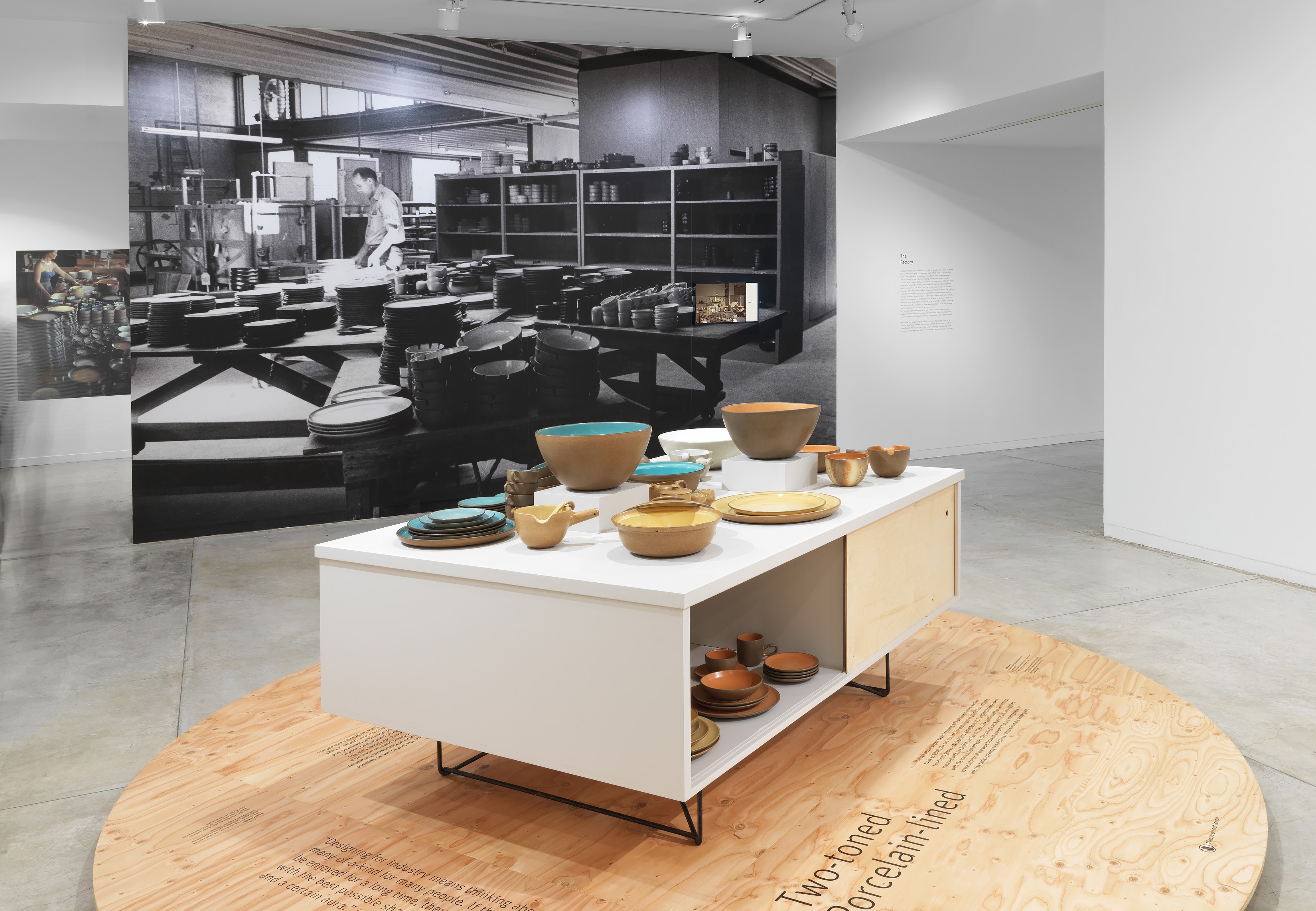 Photograph with two-toned dinnerware in the foreground and a picture of the Heath Ceramics Factory on the wall behind.