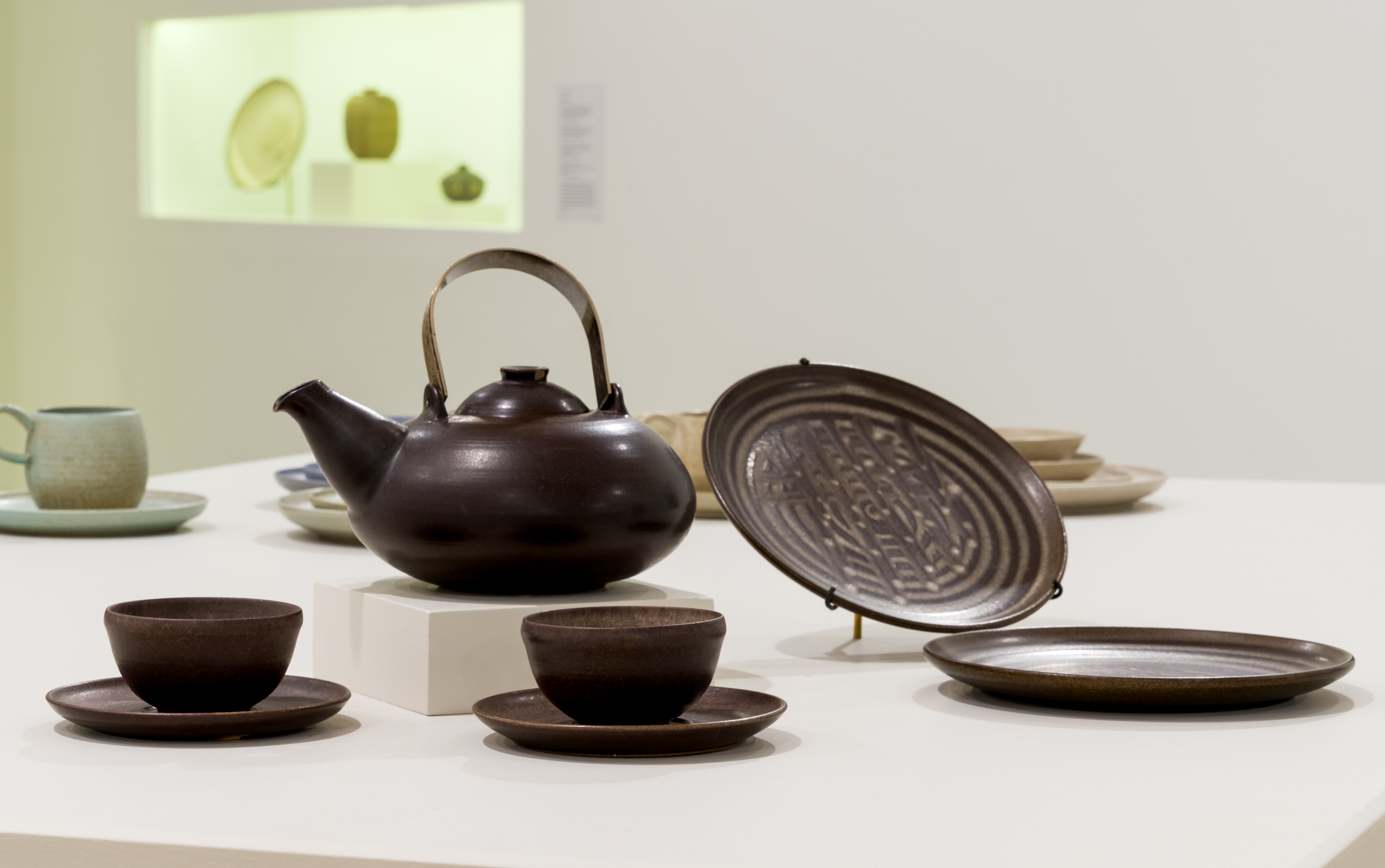Photograph of a ceramic teapot, plates and mugs in a deep purple with other pieces visible in the background.