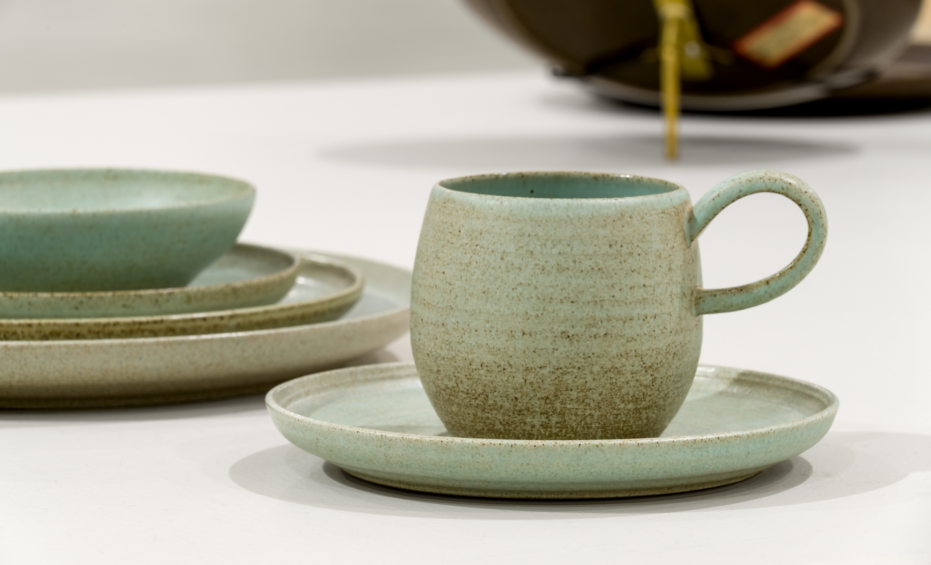 Photograph of a ceramic mug and plate set in pale green with brown specks.