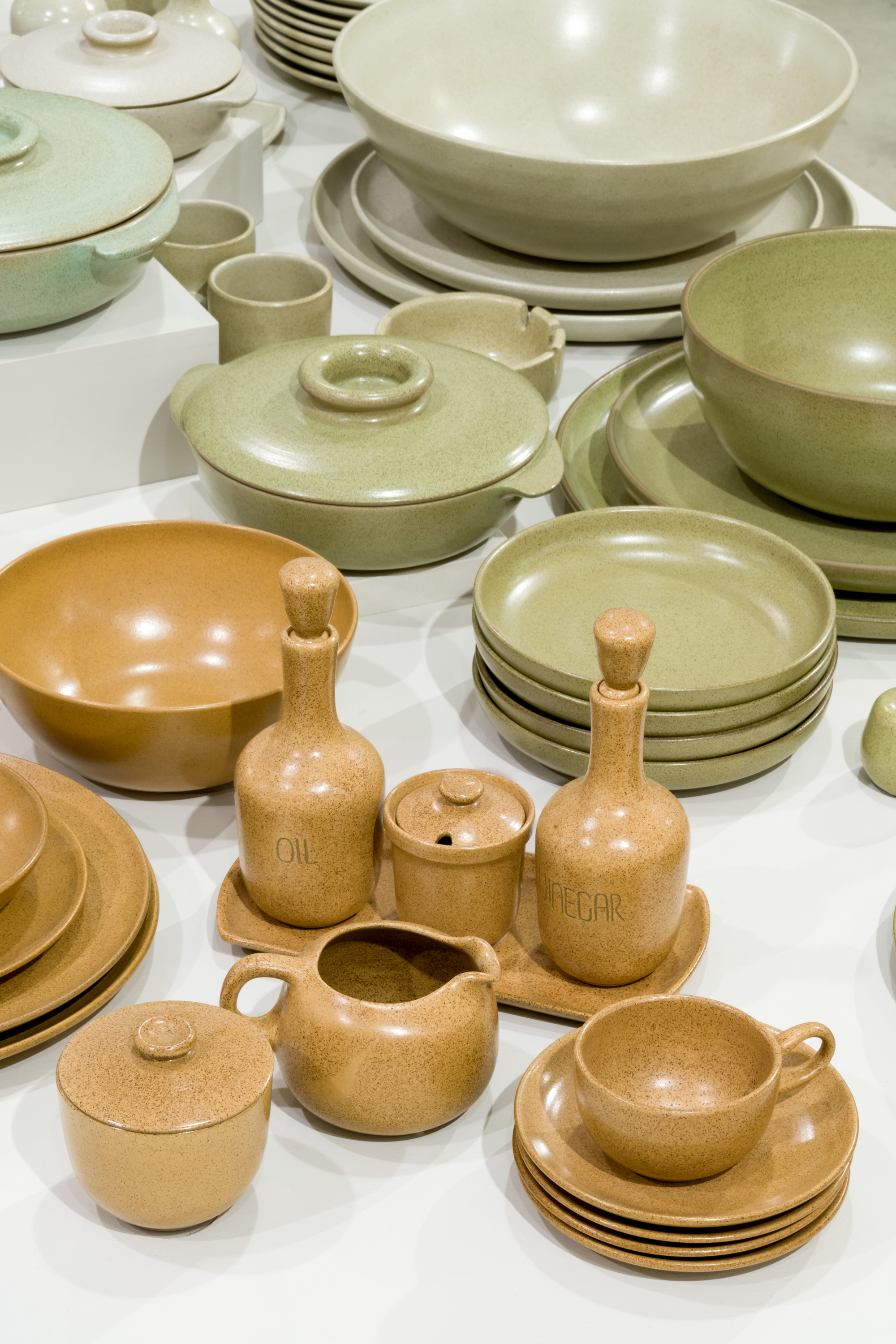 Oil and Vinegar set, bowls, plates, and jar in light orage dinnerware with light green dinnerware in the background.