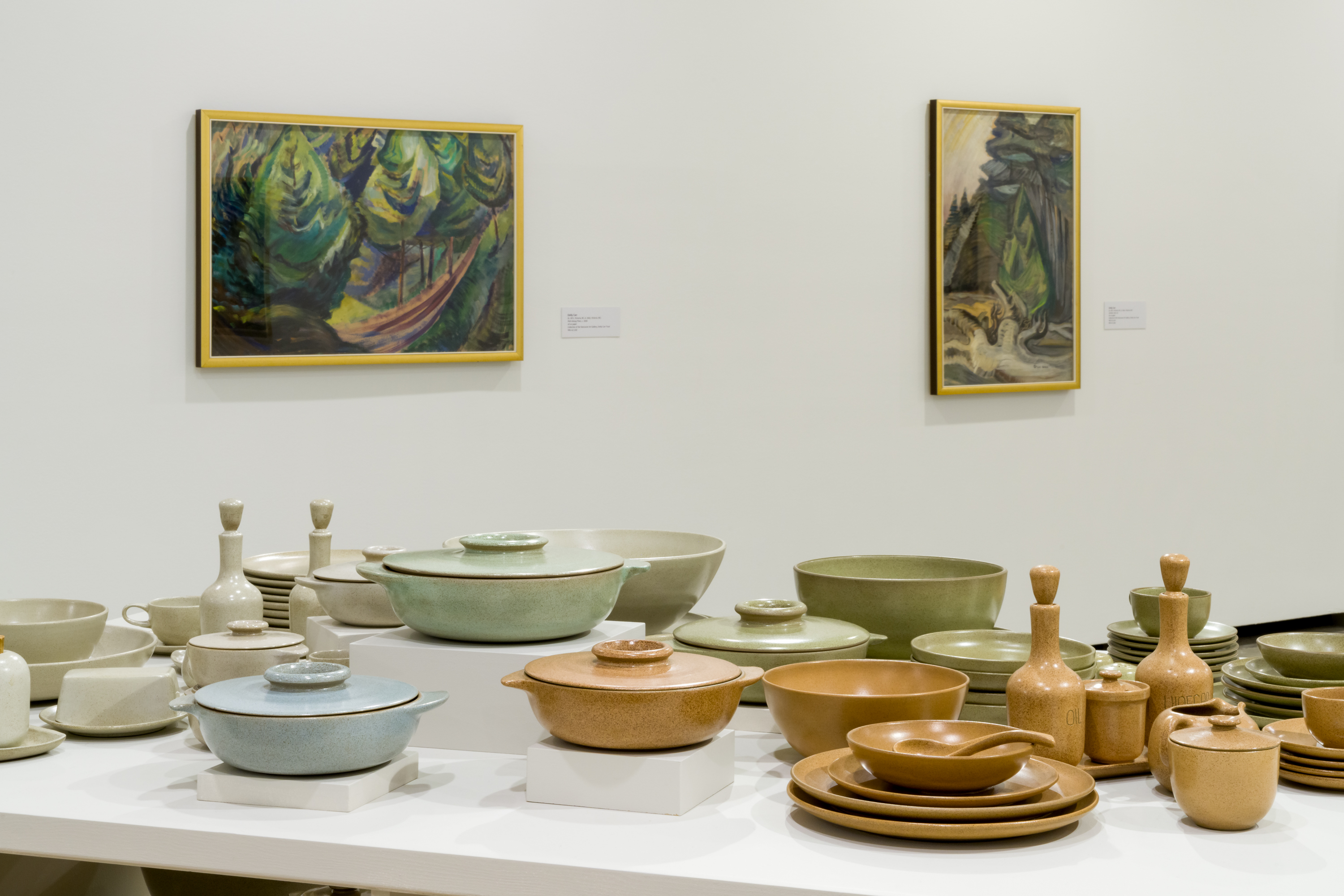 Dinnerware in light green, light blue, light orange and beige, with two paintings in the background.